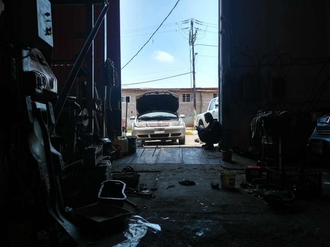 Auto mechanic inspects an open car engine in a garage.