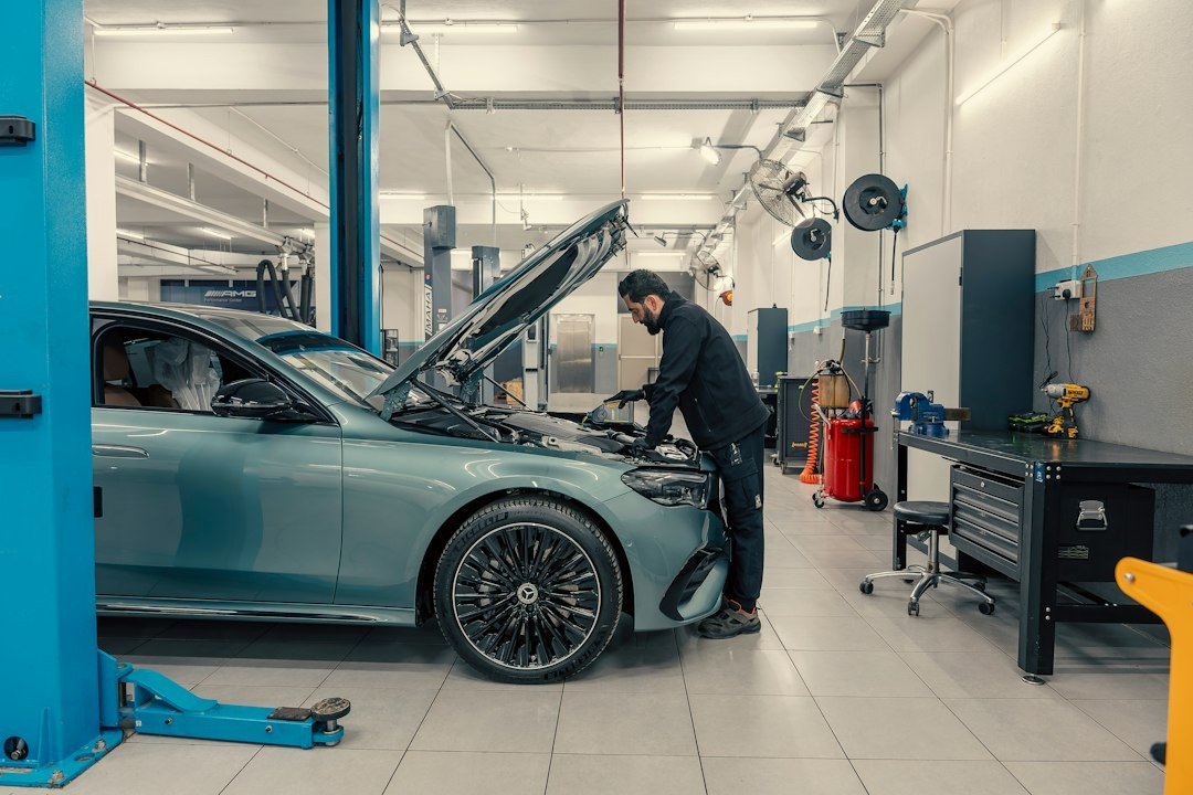 Mechanic inspecting the engine of a light blue car.